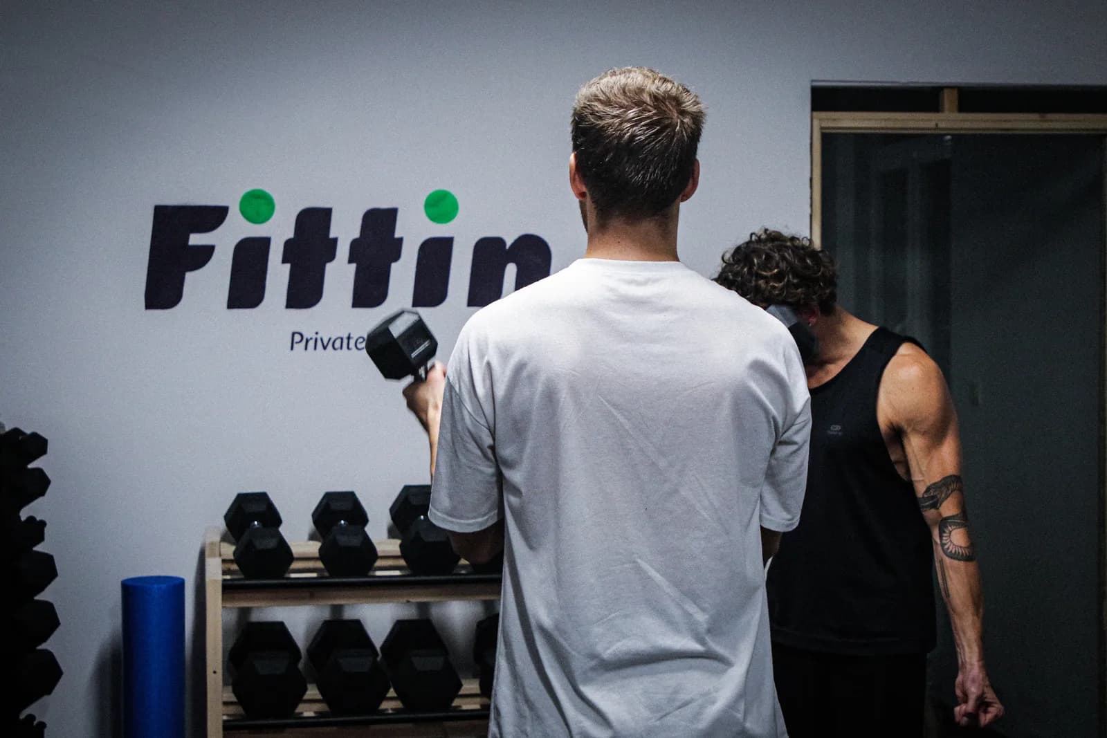 Twee leden trainen met dumbbells voor de logowand